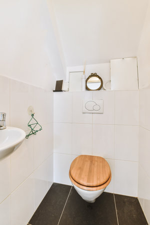 Interior of narrow restroom with sink and wall hung toilet with white walls and checkered floor