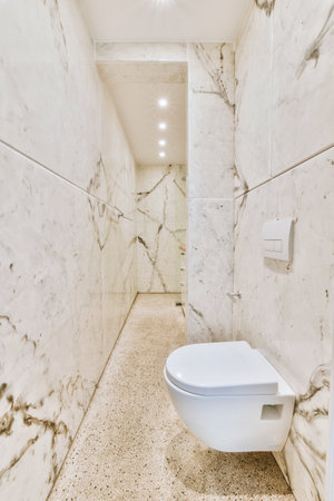 Interior of narrow restroom with sink and wall hung toilet with white walls and checkered floorの写真素材