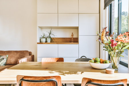 Contemporary minimalist style interior design of light studio apartment with wooden table and chairs in dining zone between open kitchen and living room with white walls and parquet floorの写真素材