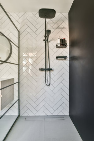 Shower faucets attached to tiled wall near glass partition and ornamental curtail in washroom at homeの写真素材