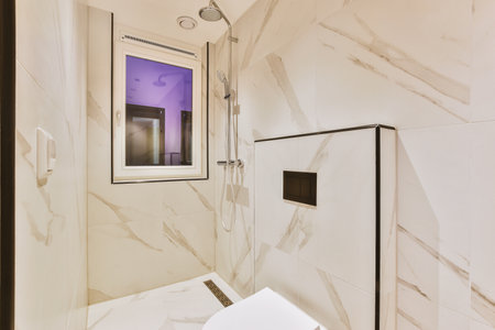 Shower faucets attached to tiled wall near glass partition and ornamental curtail in washroom at...