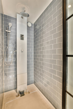 Tiled shower cabin with glass door located near sink and mirror in light restroom in contemporary...