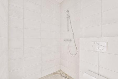 Shower faucets attached to tiled wall near glass partition and ornamental curtail in washroom at homeの写真素材