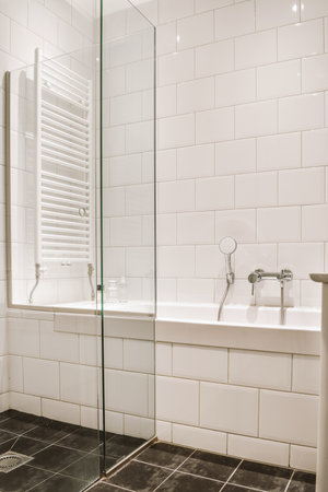 Sinks with mirrors and clean bathtub located near shower box with glass door in modern bathroom with white tiled wallsの写真素材