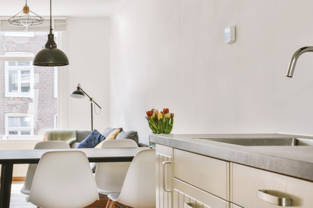 Fragment of interior of light narrow home kitchen with minimalist style white furniture with sink...