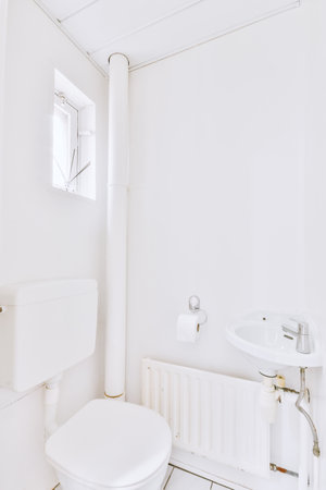 Interior of narrow restroom with sink and wall hung toilet with white walls and checkered floorの写真素材
