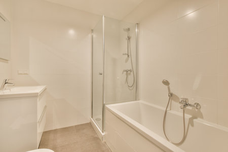 Modern flush toilet and ceramic sink installed on white tiled walls near mirror and shower box in...