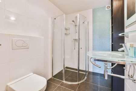 Flush toilet located between sink and shower in small tiled bathroom of contemporary apartment