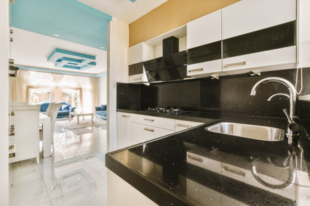 Fragment of interior of light narrow home kitchen with minimalist style white furniture with sink...