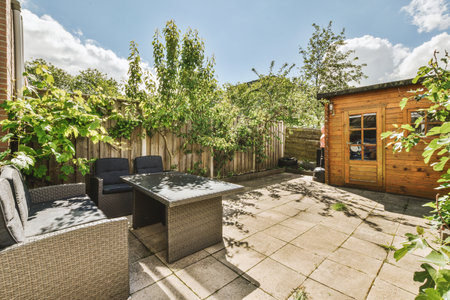 Neat paved patio with sitting area and small garden near wooden fence