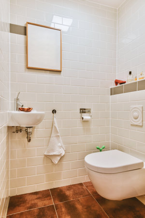 Interior of narrow restroom with sink and wall hung toilet with white walls and checkered floor
