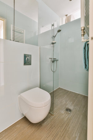 Flush toilet located between sink and shower in small tiled bathroom of contemporary apartmentの写真素材