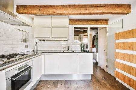 Fragment of interior of light narrow home kitchen with minimalist style white furniture with sink...