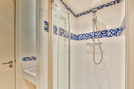 Shower faucets attached to tiled wall near glass partition and ornamental curtail in washroom at...