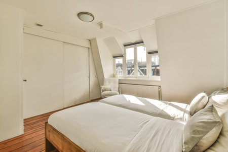 Comfortable bed placed near white wall in modern minimalist style mansard bedroom with windowsの写真素材