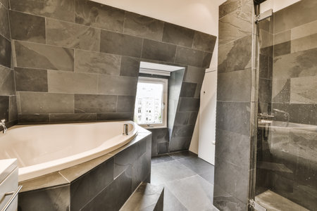 a modern bathroom with black tiles on the walls and floor, along with a white bathtub in the corner