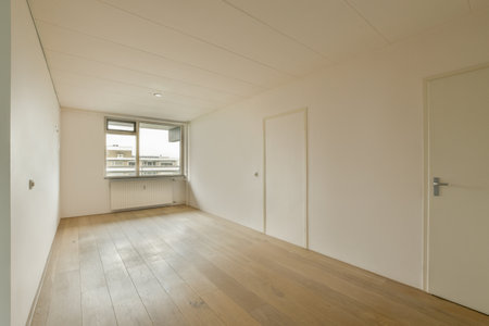 an empty room with white walls and wood flooring on the right side of the room, there is a window...