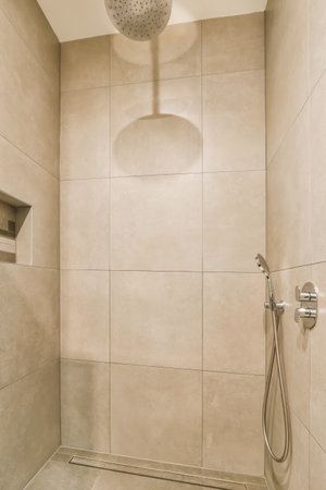 a shower room with beige tiles on the walls and floor, there is a hand held shower head in the cornerの写真素材