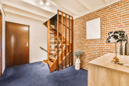 a room with brick walls and blue carpeting, including a wooden staircase leading up to the second...