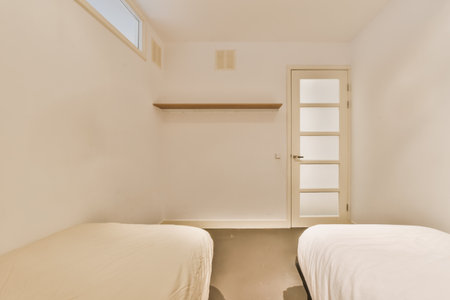 two beds in a room with white walls and wooden shelves on the wall to the right is an open door