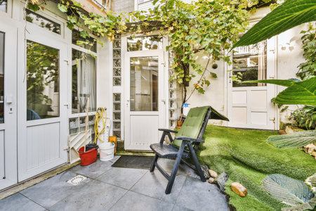 an outside area with a lawn chair and some plants on the ground next to a white door that is open