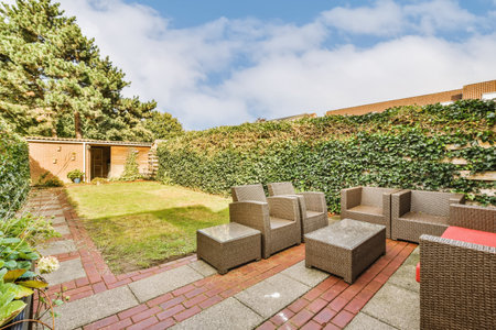 an outdoor patio area with wickers, chairs and trees in the back yard on a blue sky dayの写真素材
