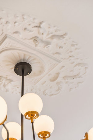 a chandel hanging on the ceiling in a room with white wallpaper and gold trim around the light...