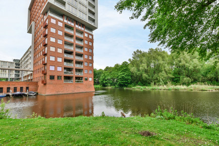 an apartment building next to a body of water with boats on the river in front and green grass around itのeditorial素材