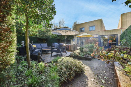 Amsterdam, Netherlands - 10 April, 2021: a backyard area with some plants and an umbrella in the middle part of the yard, surrounded by trees and bushesのeditorial素材