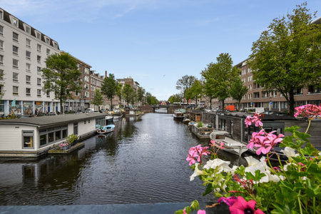 Amsterdam, Netherlands - 10 April, 2021: a canal with boats and flowers in the fore, as seen from a bridge over looking at buildings on either sideのeditorial素材