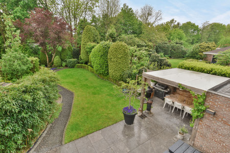 Amsterdam, Netherlands - 10 April, 2021: the back garden with an outdoor dining table and chairs, surrounded by lush green trees on a blue sky dayのeditorial素材