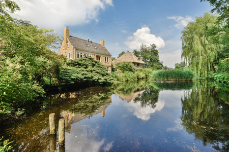 a house on the waters edge with trees in the background and blue sky reflected in the water surfaceのeditorial素材