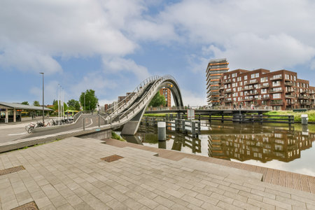 a bridge over the water with buildings in the background and people sitting on benches at the other side of the riverのeditorial素材