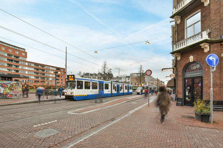 Amsterdam, Netherlands - 10 April, 2021: people walking on the street in front of a train and some buildings that are behind them, with blue skysのeditorial素材