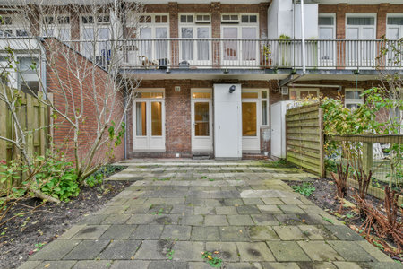 Amsterdam, Netherlands - 10 April, 2021: an outside view of a house with trees and plants in the front yard, surrounded by brick walls on either sideのeditorial素材