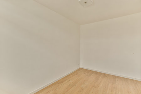 an empty room with white walls and wood flooring the wall is painted in light beige, there is a ceiling fanの写真素材