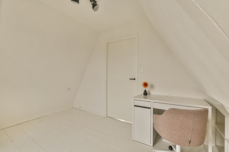 a room with white walls and wood flooring, including a small desk in the corner on the right sideの写真素材