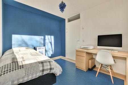 a bedroom with a bed, desk and computer monitor on the wall in front of the room is bright blue