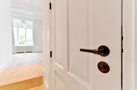 a door handle on a white door with wood floors in the background and an empty room to the right sideの写真素材
