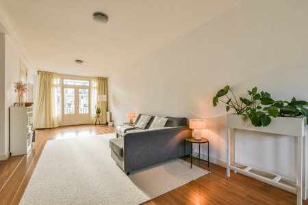 a living room with white walls and hardwood flooring, there is a grey couch in front of the sofaの写真素材