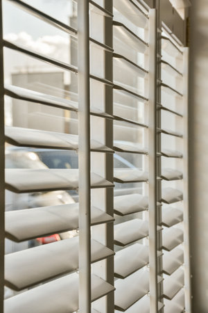 white blinds in a window with cars parked on the other side of the building behind it is an empty parking lotの写真素材