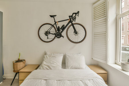 a bicycle mounted on the wall above a bed in a bedroom with white sheets, pillows and a wooden benchの写真素材