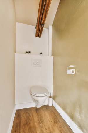 a toilet in the corner of a room with wood flooring and walls painted white, there is a light fixture on the wallの写真素材