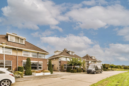 some houses with cars parked on the side of the road and clouds in the sky above them are white fluffy cloudsの写真素材