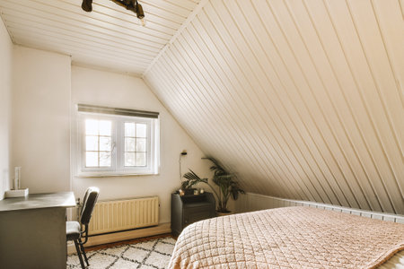 a bedroom with a bed, desk and window in the corner of the room on the right is a chairの写真素材