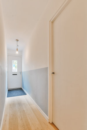 an empty hallway with wood floors and white walls, the door is open to reveal a light blue area in...