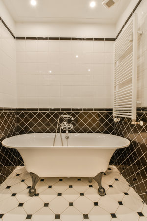 a bathroom with black and white tiles on the walls, floor, and bathtub in its cornerの写真素材