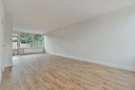 an empty room with wood flooring and white paint on the walls, there is a large window in the cornerの写真素材