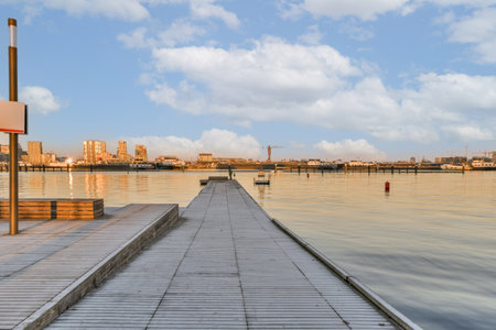 a pier in the middle of a body of water with buildings in the background and blue sky above it,の写真素材