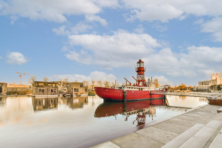 a red boat in the water with buildings in the background and clouds in the sky overcasted by blue skiesの写真素材